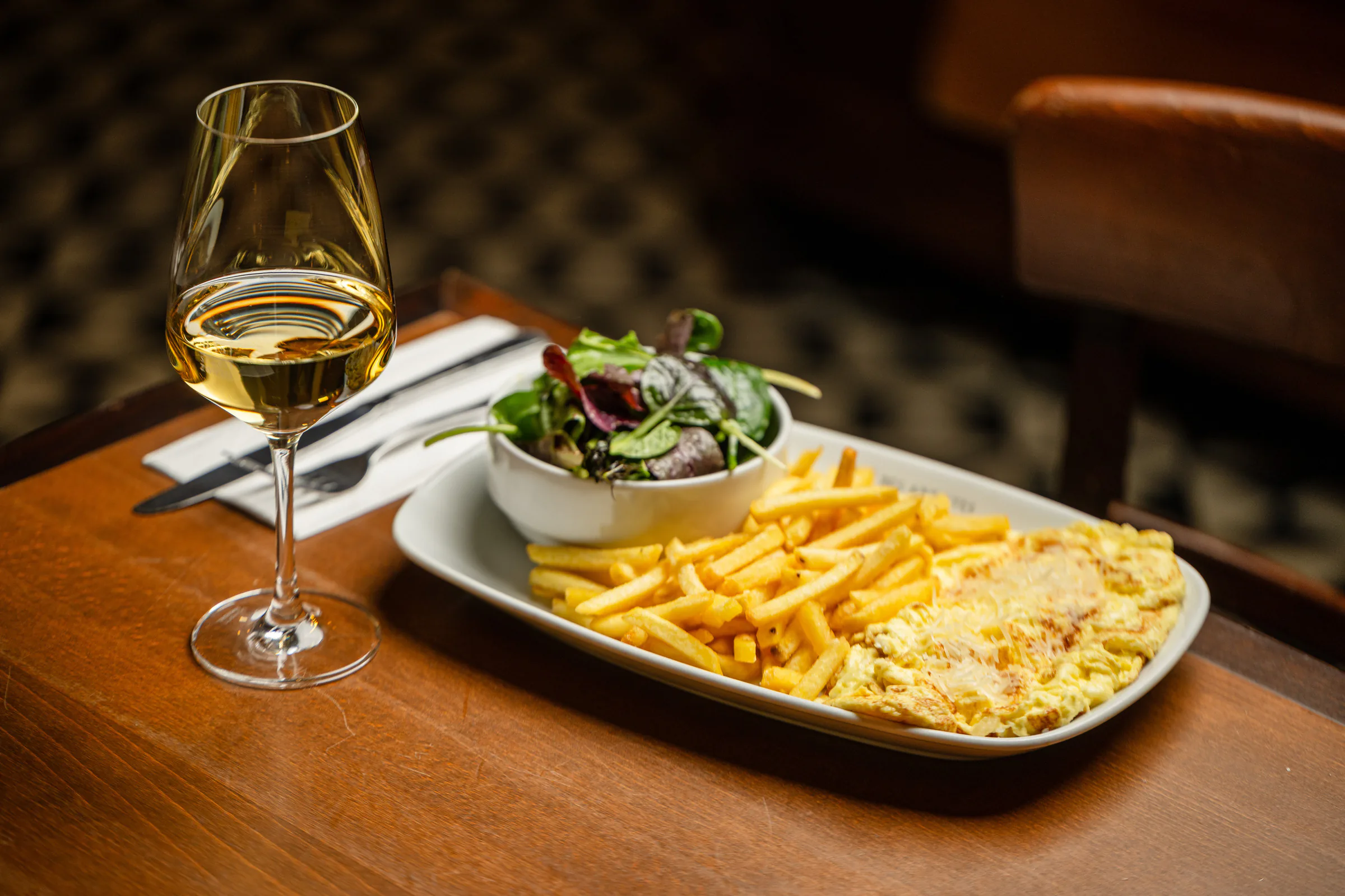 Omelette mit Pommes frites, Salat und einem Glas Weißwein